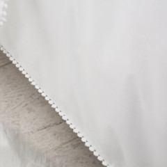 Dichtbijzicht van een wit bed met een frisse, witte kussenhoes met een afwerking van kleine bolletjes, stralend in natuurlijk licht.