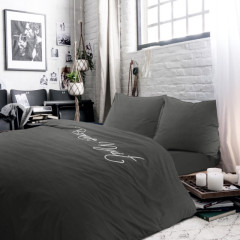 Een bed met een zwart dekbed met opdruk 'bonne nuit' en bijpassende kussens, uitnodigend en stijlvol ingericht.