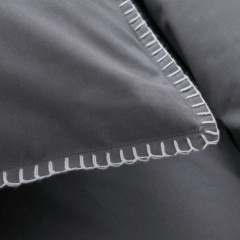 Grijs kussen met witte stiksels in close-up, dat comfort en elegantie uitstraalt.