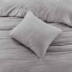 Een zacht kussen ligt op een bed met een grijze deken eroverheen, klaar voor een comfortabele nachtrust..