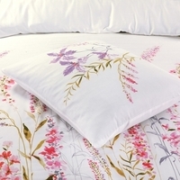 Een bed met een wit dekbed en paarse bloemen, dat een vrolijke en uitnodigende uitstraling heeft.