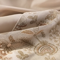 Dichtbijopname van een beige en gouden bloemenpatroon op stof, met delicate details en een elegante uitstraling.