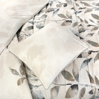 Een bed met een modern bladmotief in wit en beige, dat een frisse en uitnodigende sfeer in de kamer creëert.