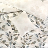 Een bed bedekt met een wit en beige bladmotief, dat een frisse en moderne sfeer in de slaapkamer creëert.