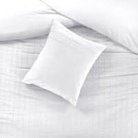 Een wit bed met een kussen en een witte dekbed, netjes opgemaakt in een lichte slaapkamer.