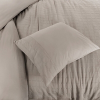 Een bed met een zacht zandkleurig kussen en een stijlvolle kussensloop, uitnodigend voor ontspanning.