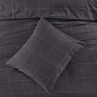 Zwarte bedspread met blokken en een kussen, die samen een strakke en elegante look voor het bed creëren.